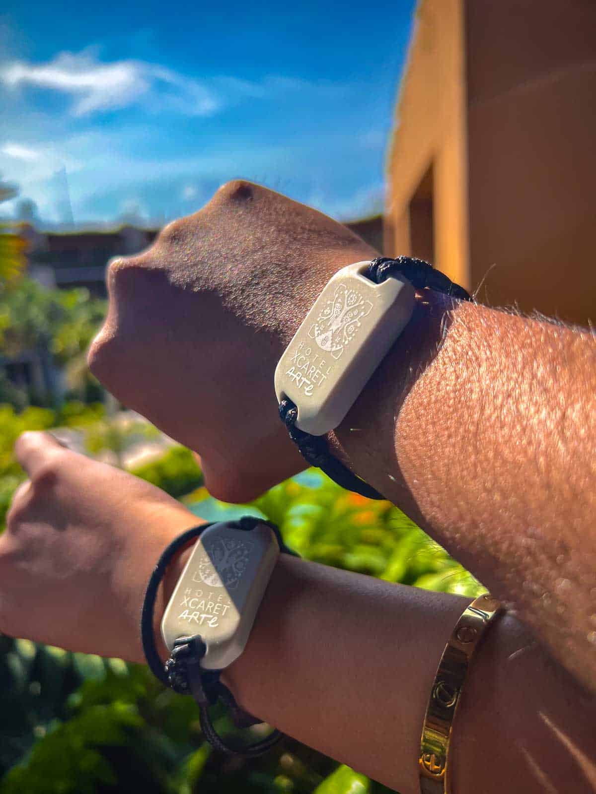 Two arms wearing Xcaret Arte grey wristbands.The wristbands have a leather bracelet, and rubber center.