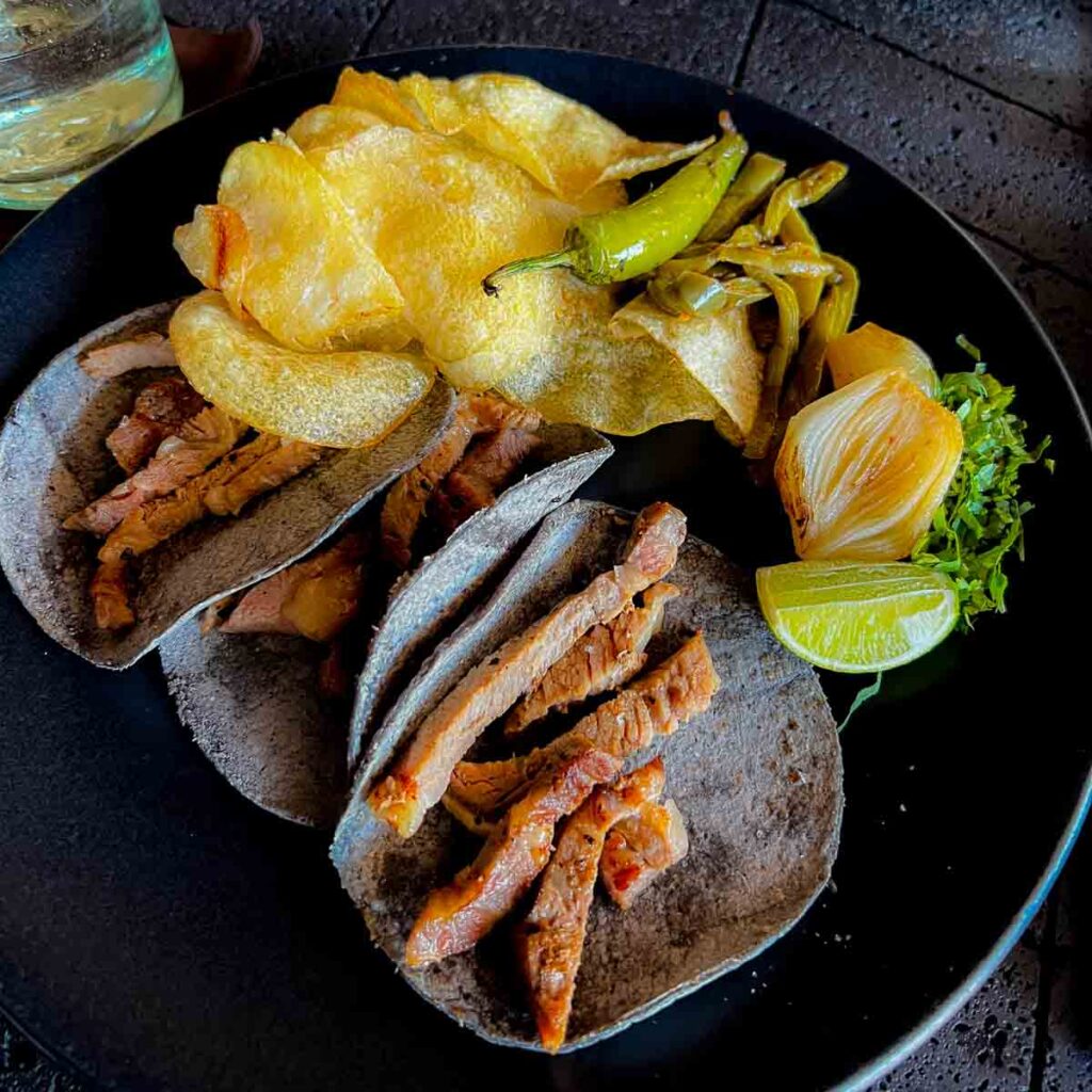 A close up of steak tacos in black tortillas on a black plate.
