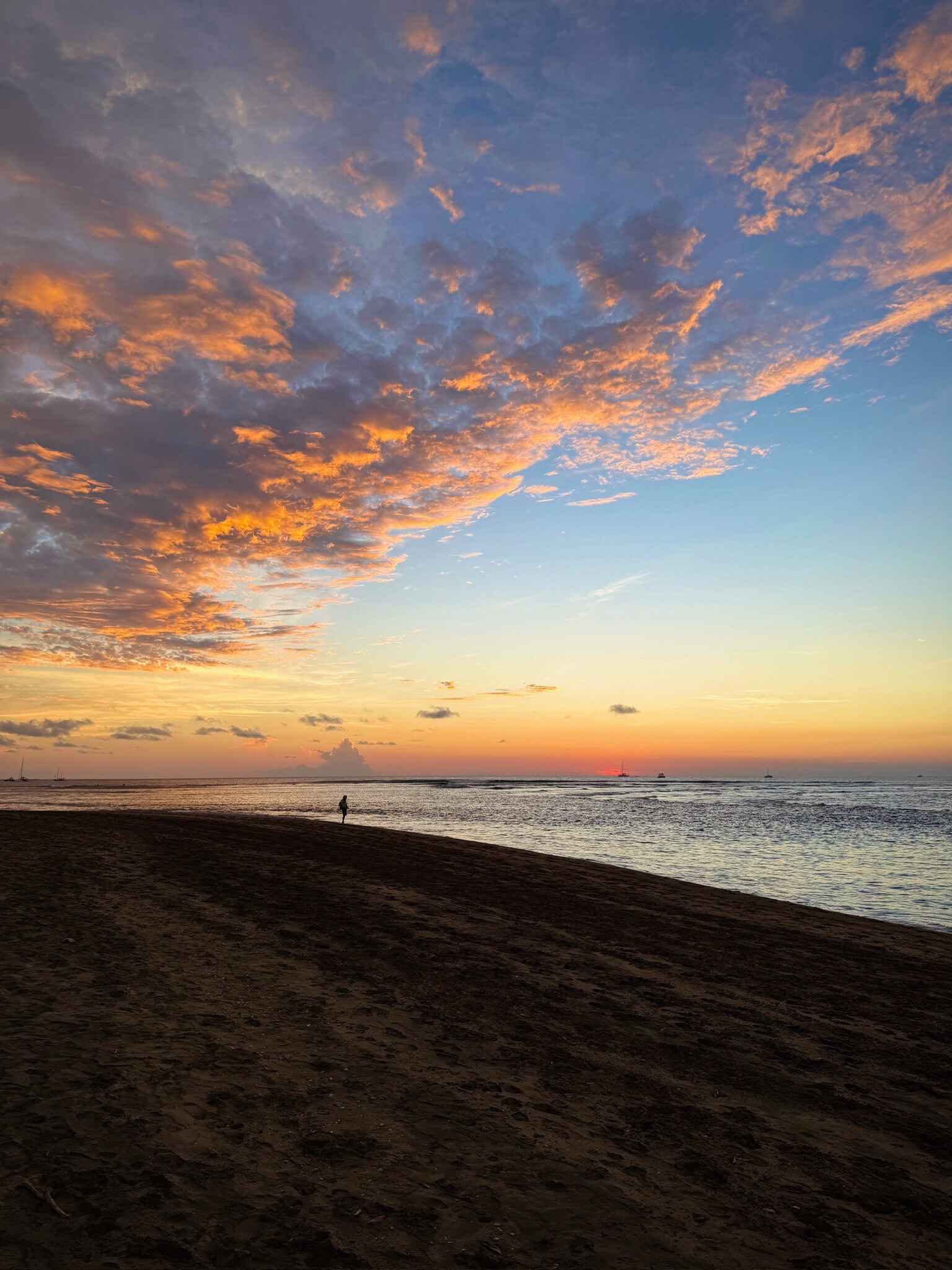Riz standing alone in on Tamarindo Beach just as the sun has set. The beach is empty and the sky looks dramatic with clouds and the colors of sunset.
