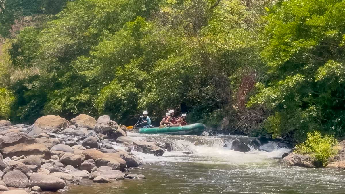 A green raft with three passengers going over some rapids in Tenorio River. A shot taken during the Tenorio White Water Rafting tour in Costa Rica.