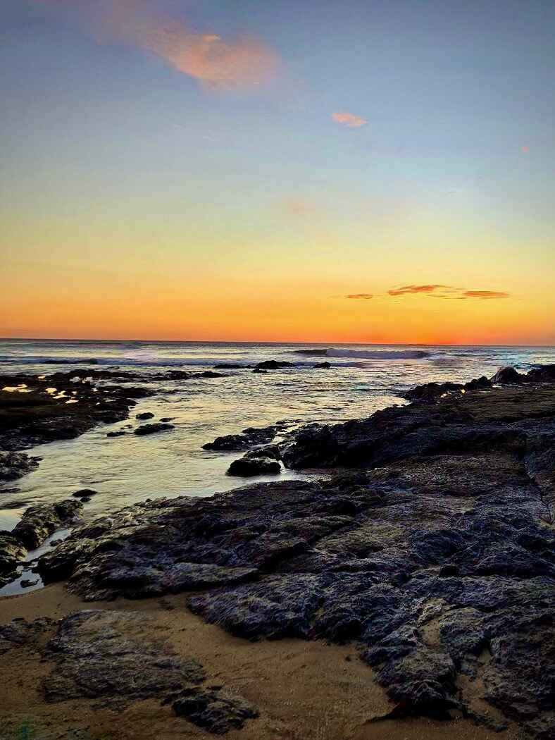 The rocks in Playa Langosta just after sunset. The water looks a bit choppy, but the beach and waters are empty and the colors of the sunset look lovely in the horizon.