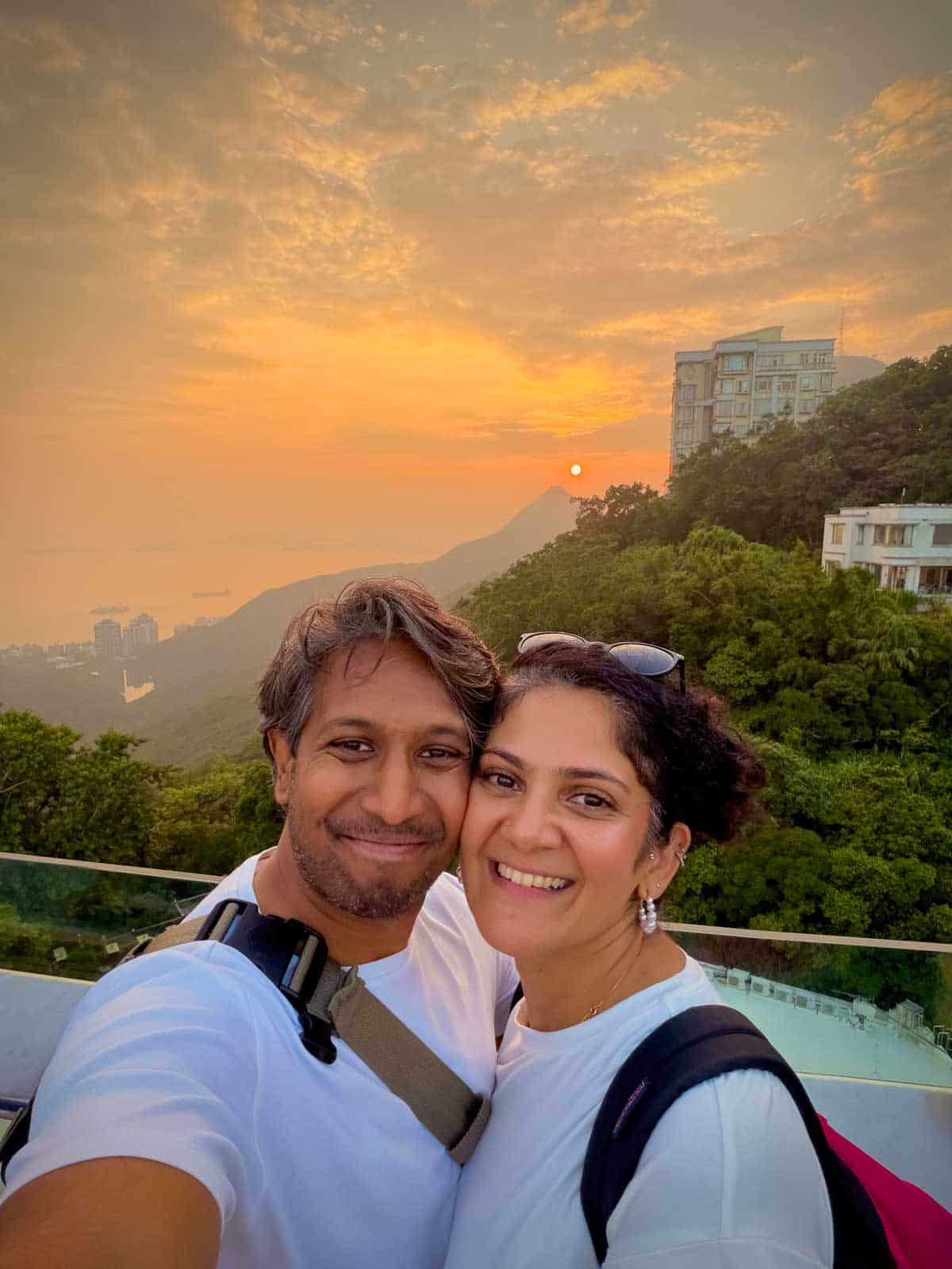 Riz & Reem watching an orange sunset over wooded hills and the sea from Victoria Peak.