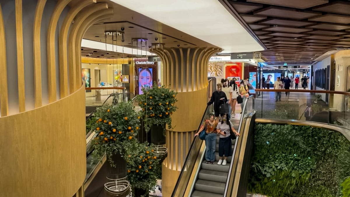 Shoppers on escalators inside K11 MUSEA, surrounded by curved wooden columns, indoor trees and a green wall.