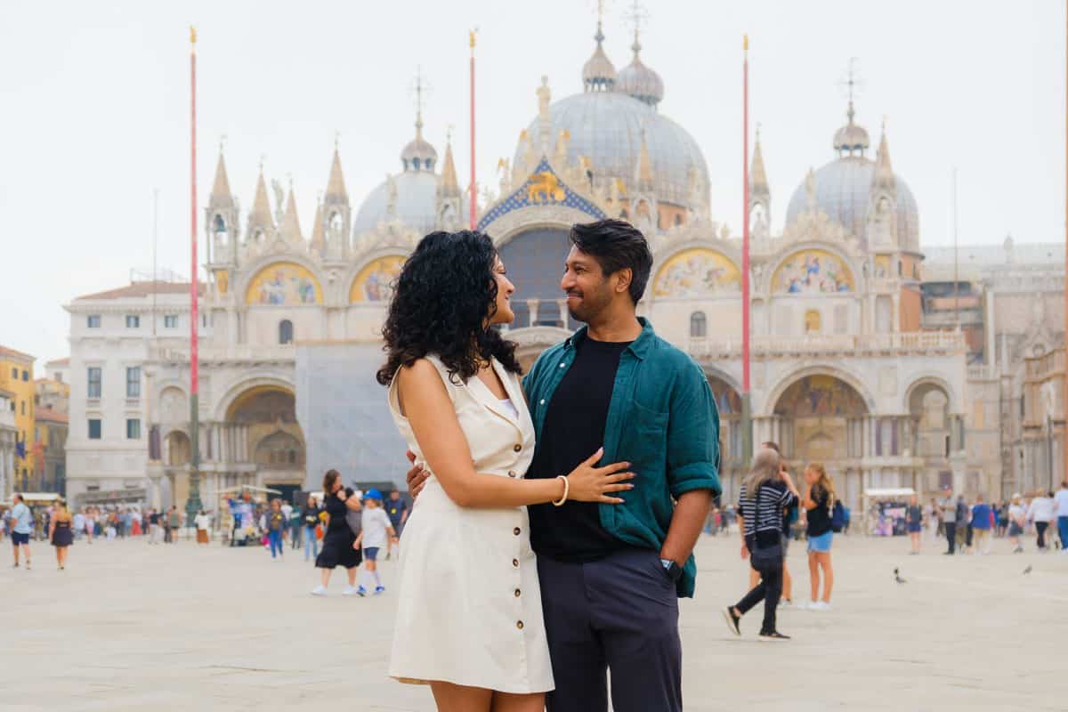 Riz and Reem standing looking at each other fondly in St. Mark's Square in front of St. Mark's Basilica - Venice, Italy.