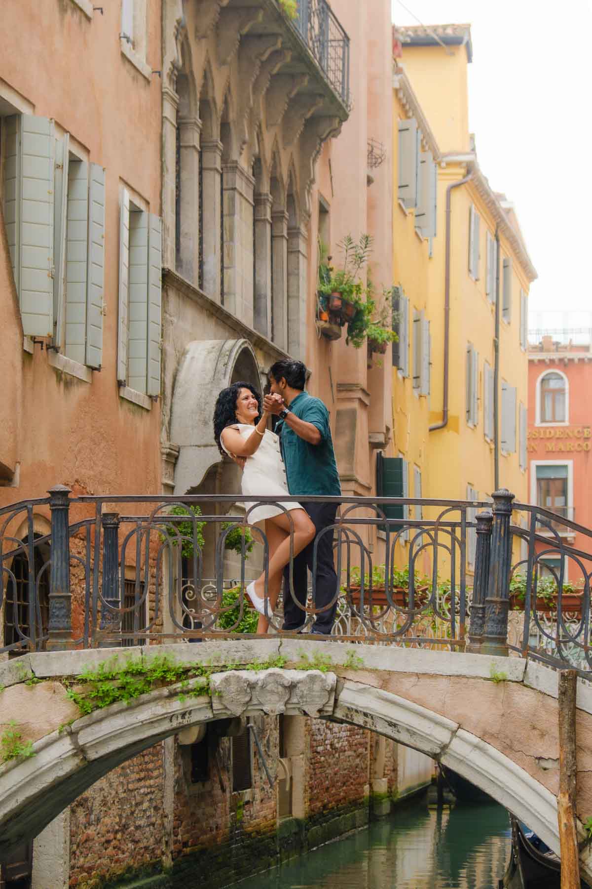 Riz and Reem dancing on a small bridge over a canal in Venice. Reem is laughing as Riz dips her.