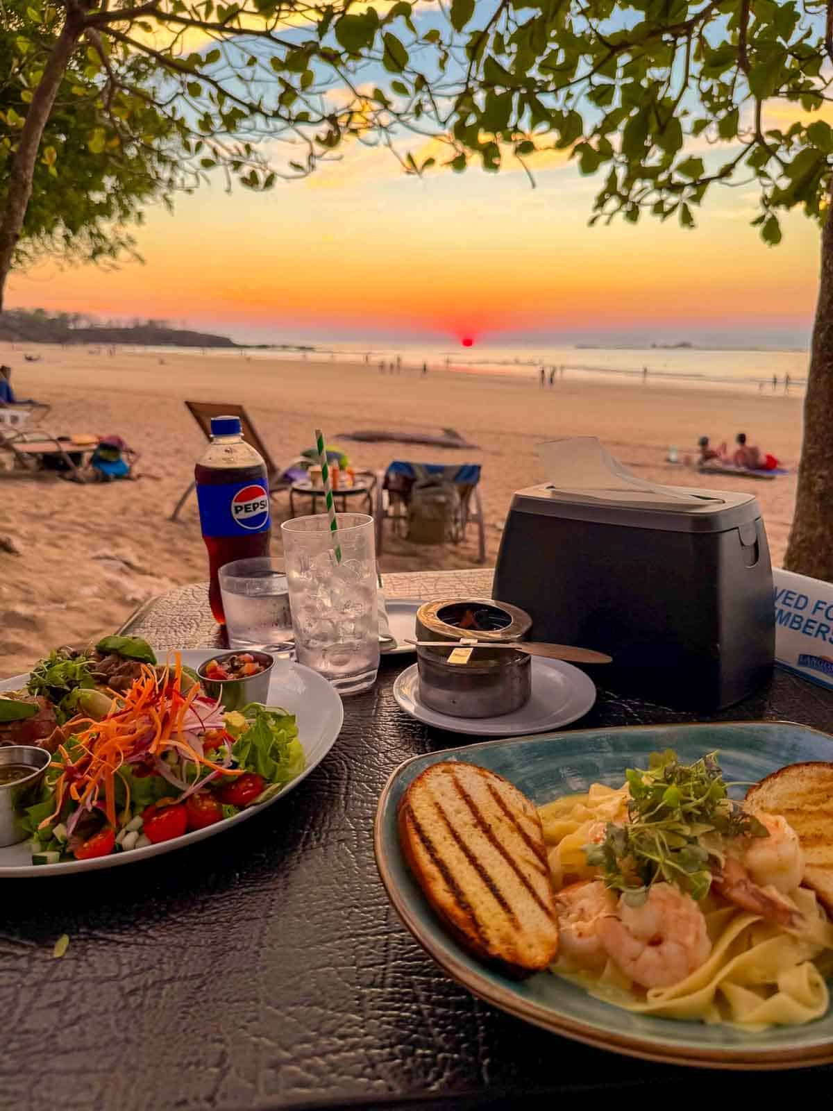Shrimp pasta and salad served at a beachfront table during sunset at Langosta Beach Club